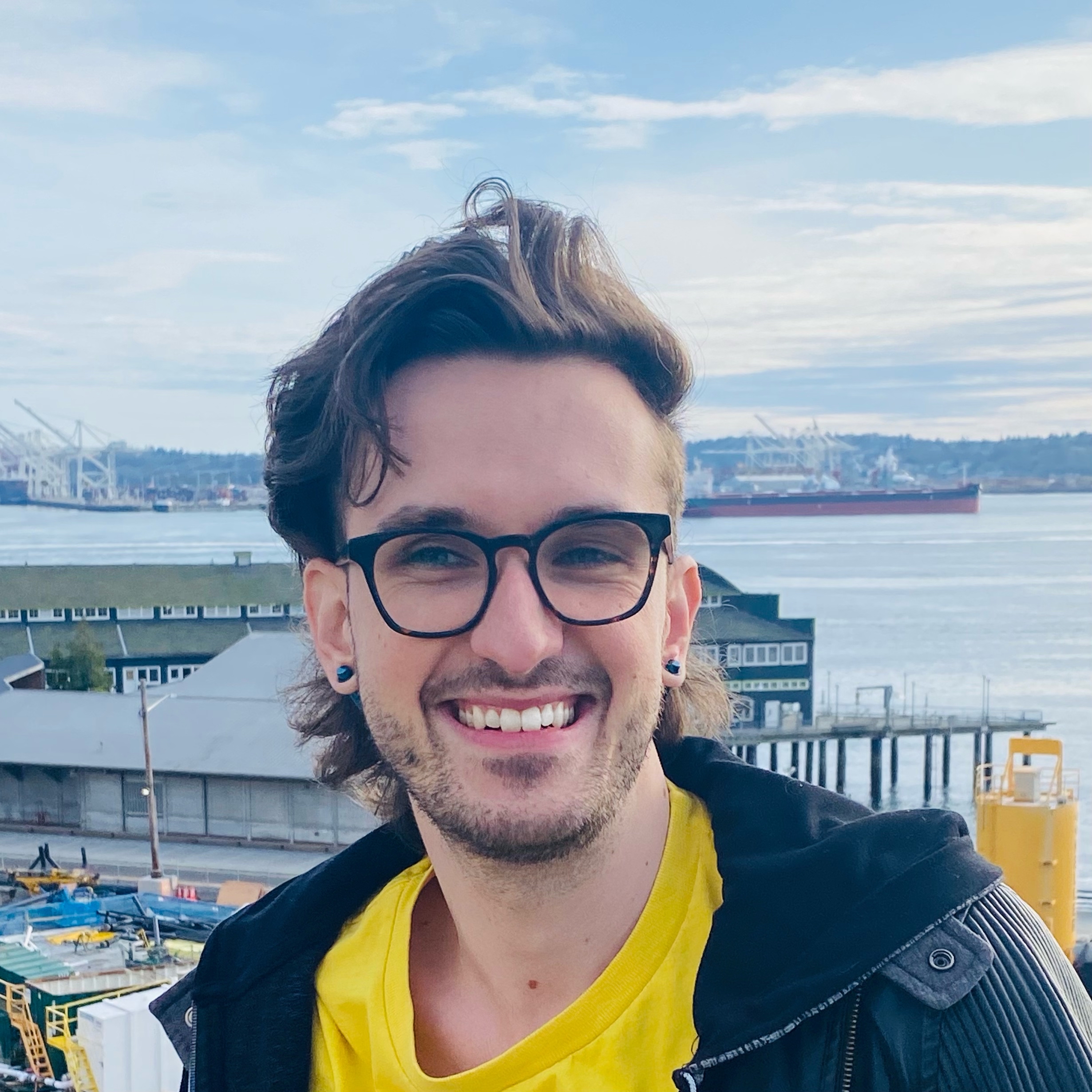 picture of androgenous light-skinned person in front of the Puget Sound with dark brown hair, smiling