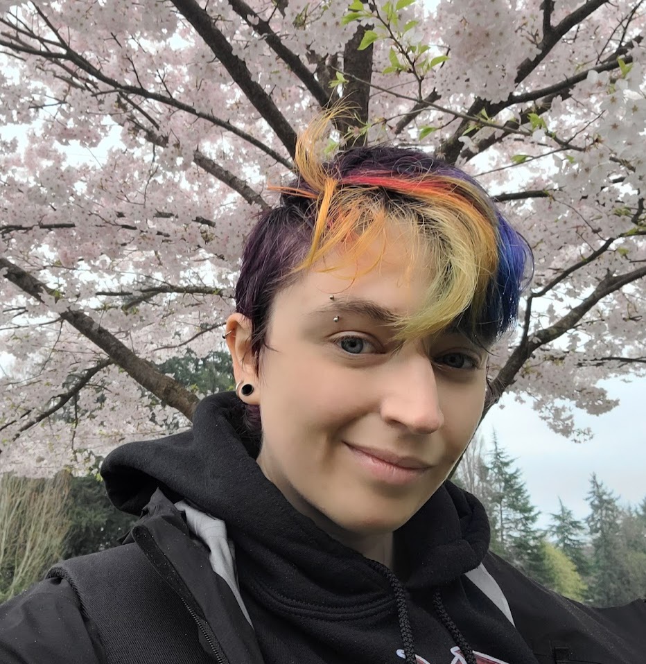 picture of androgenous light-skinned person in front of cherry blossoms with rainbow colored hair